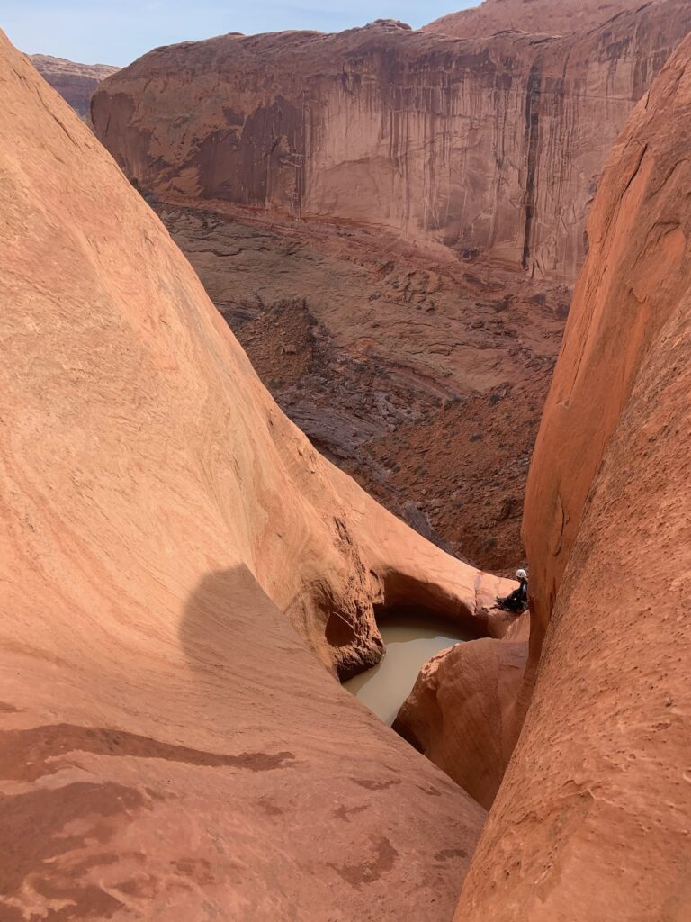 Image of a vast Utah canyon with a lone canyoneer sitting on the precipice. 